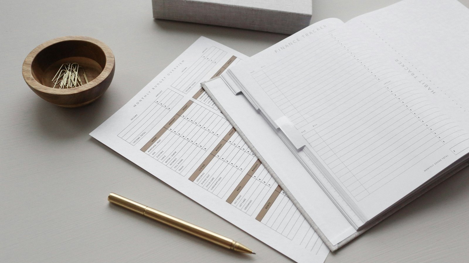 A desk flatlay of a budget planner and habit tracker with a pen and paperclips