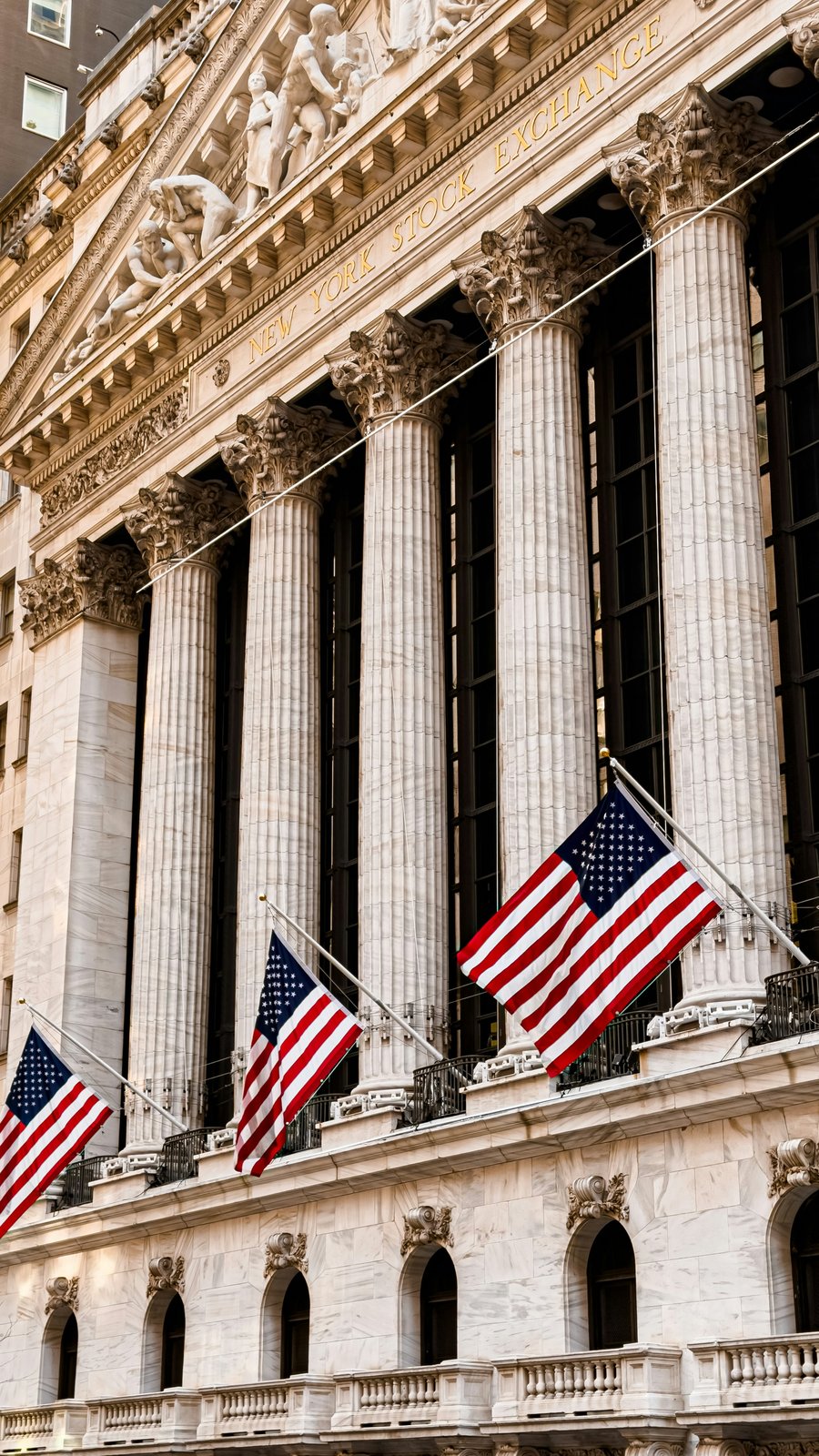 A close-up diagonal view of the New York Stock Exchange columns and American flags